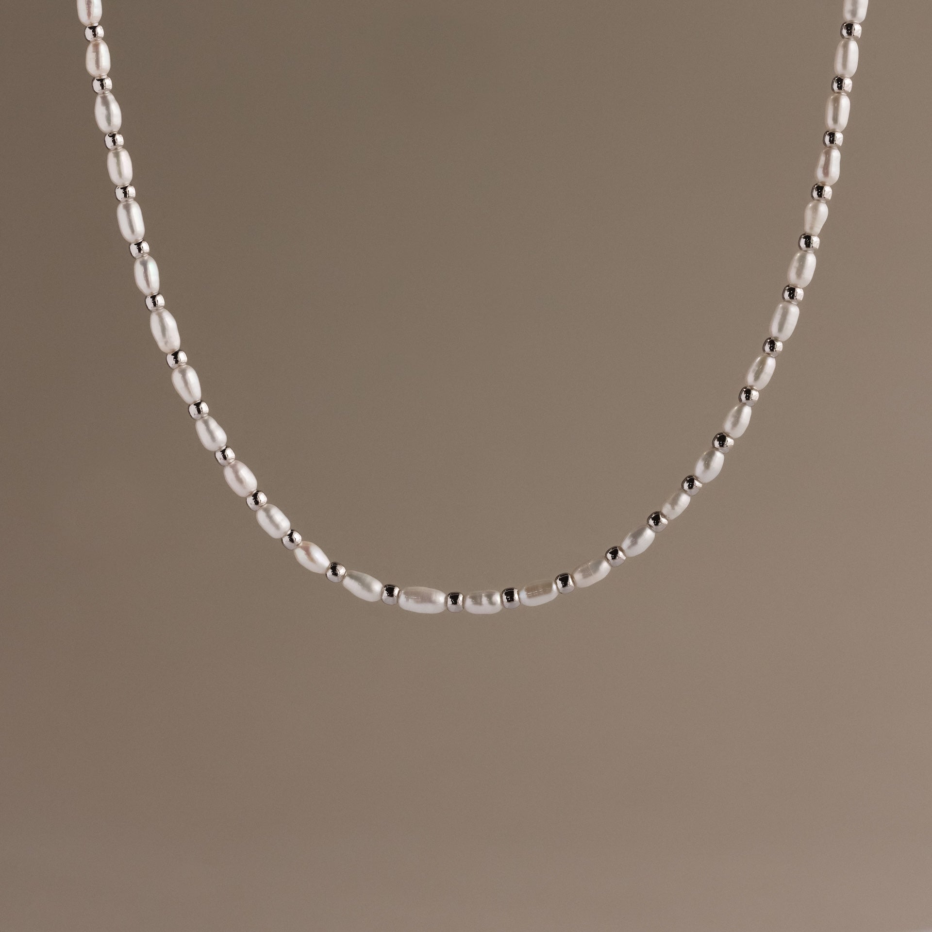 The Beaded Pearl Necklace in White Gold features polished beads displayed against a plain taupe background.