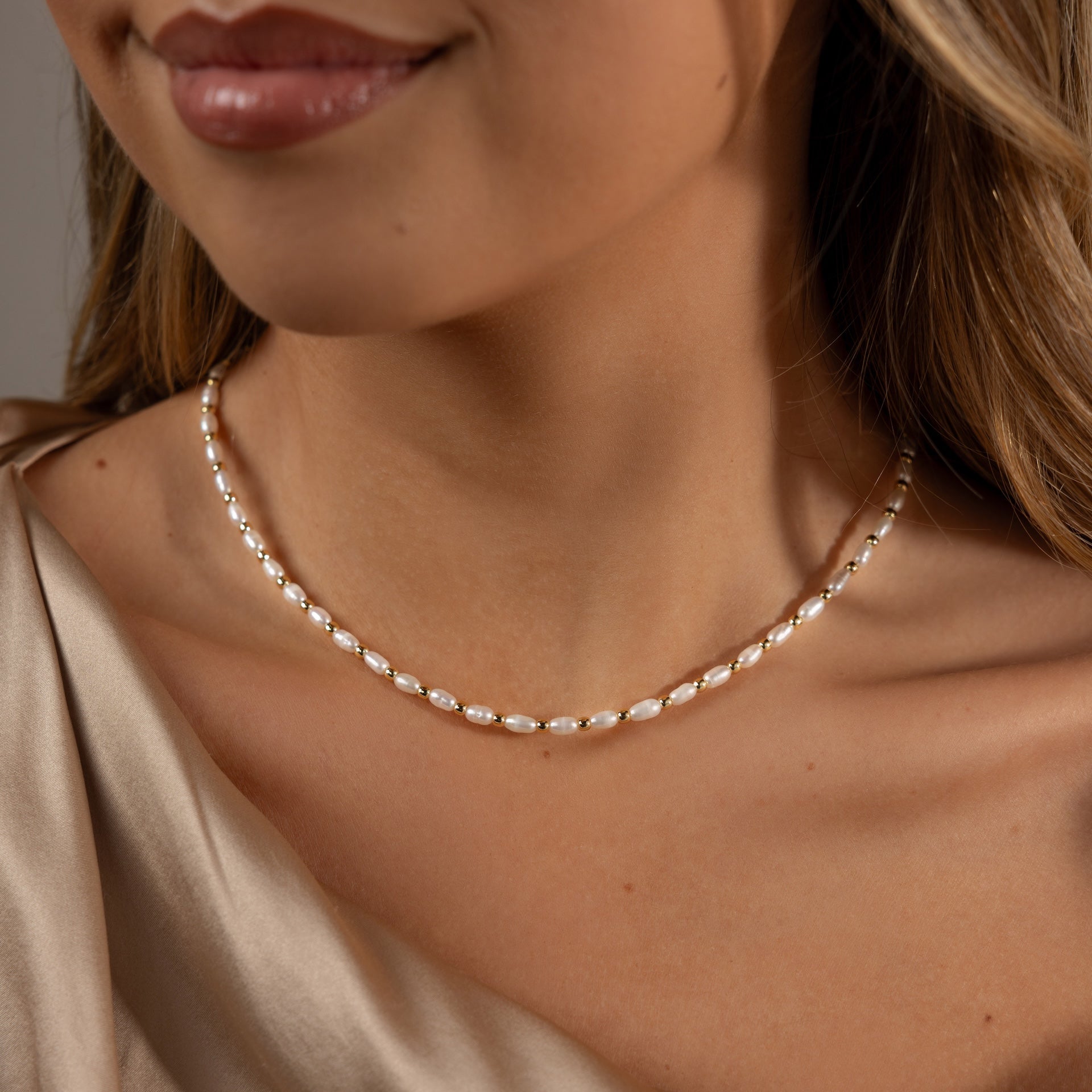 A woman models the Beaded Pearl Necklace, crafted with delicate polished beads, paired with a beige satin top, highlighting her neck and part of her face.