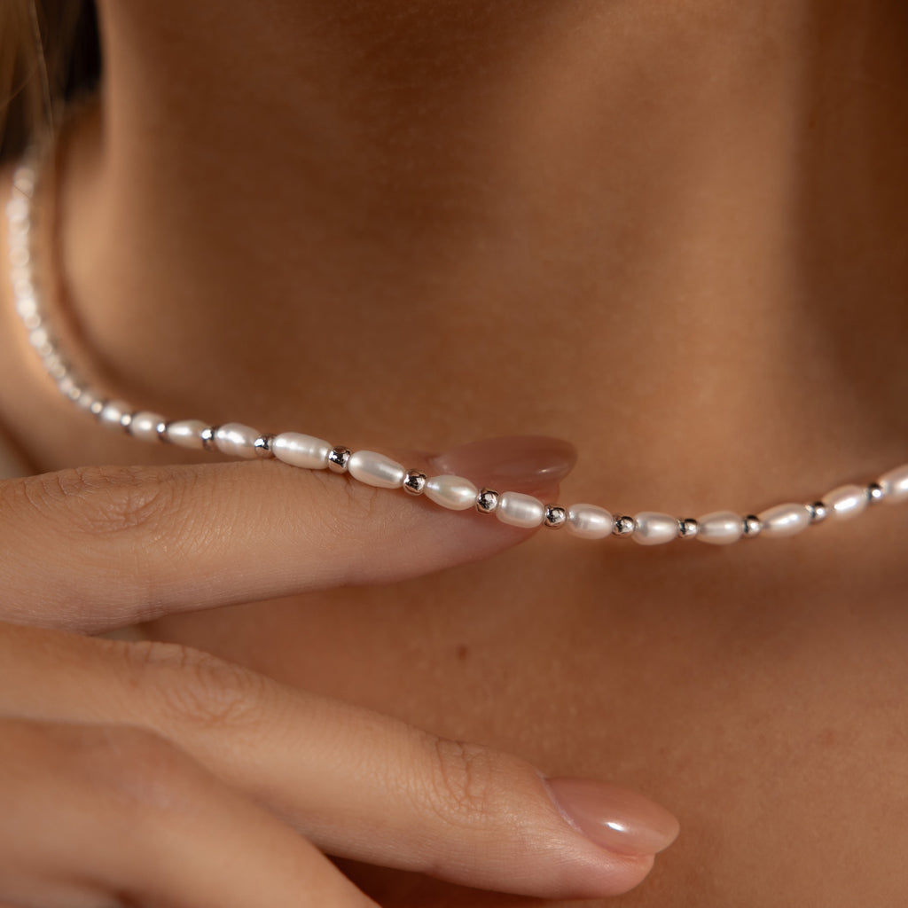 A hand touches the Beaded Pearl Necklace, adorned with freshwater pearls and delicate polished beads that rest gracefully on a neck.
