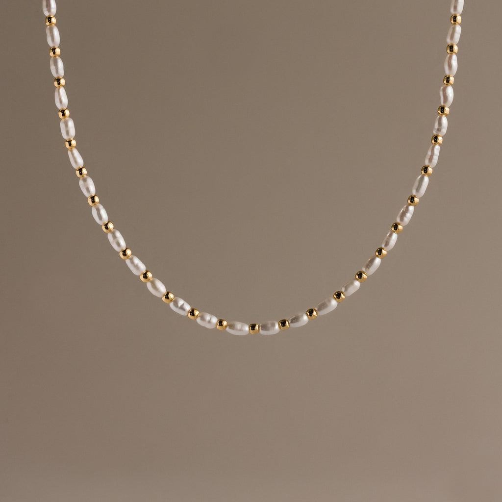 The Beaded Pearl Necklace in 18K Gold showcases alternating small freshwater pearls and polished gold beads, set against a plain beige background.