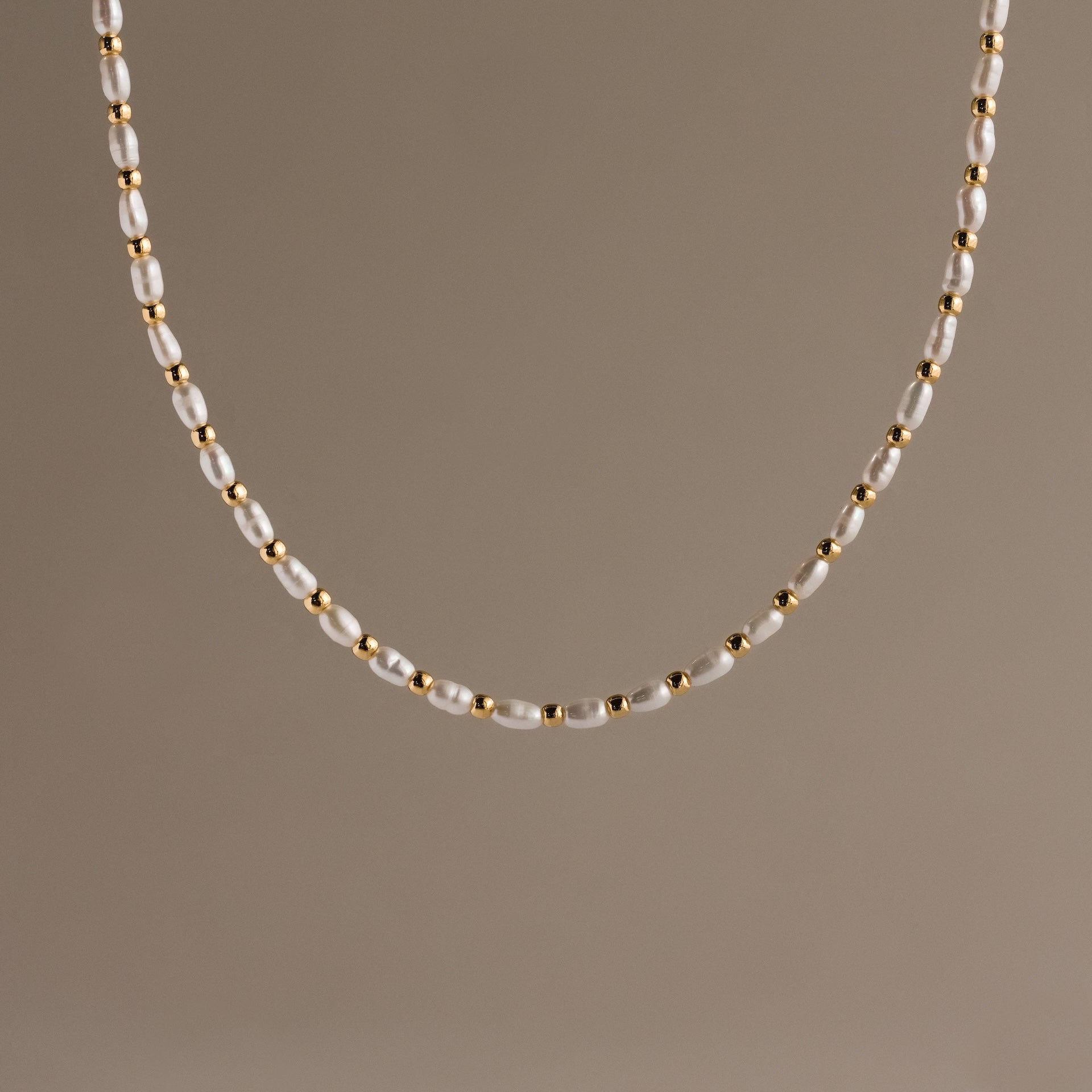The Beaded Pearl Necklace in 18K Gold showcases alternating small freshwater pearls and polished gold beads, set against a plain beige background.