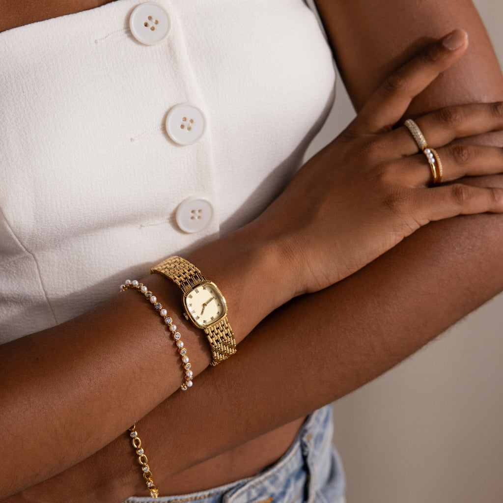 Woman in white top wearing the Pave Woven Timepiece watch, bracelet, and rings, arms crossed and dressed in light blue jeans.