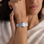 A woman wearing the Pave Scalloped Timepiece in White Gold, featuring a scallop-link bracelet and pavé bezel, rests her hand near her face.