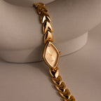 Geometric Oval Timepiece wristwatch with an oval-shaped dial and leaf-link band, displayed on a curved, light-colored surface.