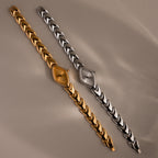 Gold and silver geometric oval watches with chevron-link bands on a neutral background.
