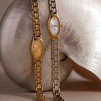 The Slim Oval Timepiece with its polished link bracelet leans gracefully against a large, shiny seashell.