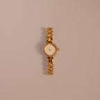 The Heart Link Timepiece is a gold wristwatch featuring heart-shaped links and a minimalist dial, displayed on a light beige background.