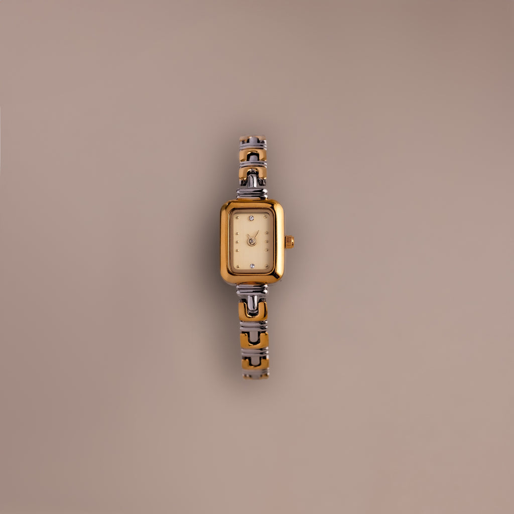 The Azteca Link Timepiece in Mixed Metal, featuring a rectangular case, patterned band, and minimalist champagne dial, rests on a plain beige background.