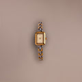 The Azteca Link Timepiece in Mixed Metal, featuring a rectangular case, patterned band, and minimalist champagne dial, rests on a plain beige background.