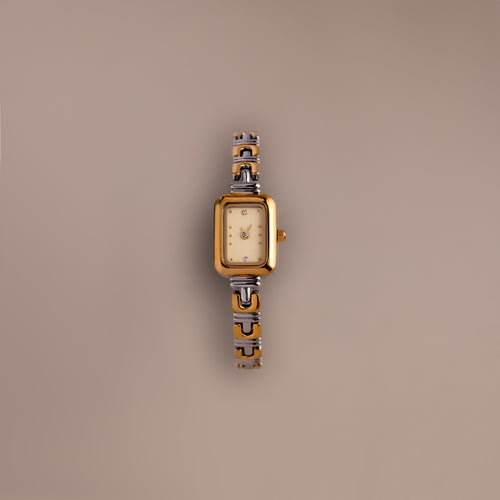 The Azteca Link Timepiece in Mixed Metal, featuring a rectangular case, patterned band, and minimalist champagne dial, rests on a plain beige background.