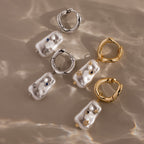 Starry Baroque Pearl Charm Hoops featuring pearl and gemstone accents are displayed on a beige, wavy surface.