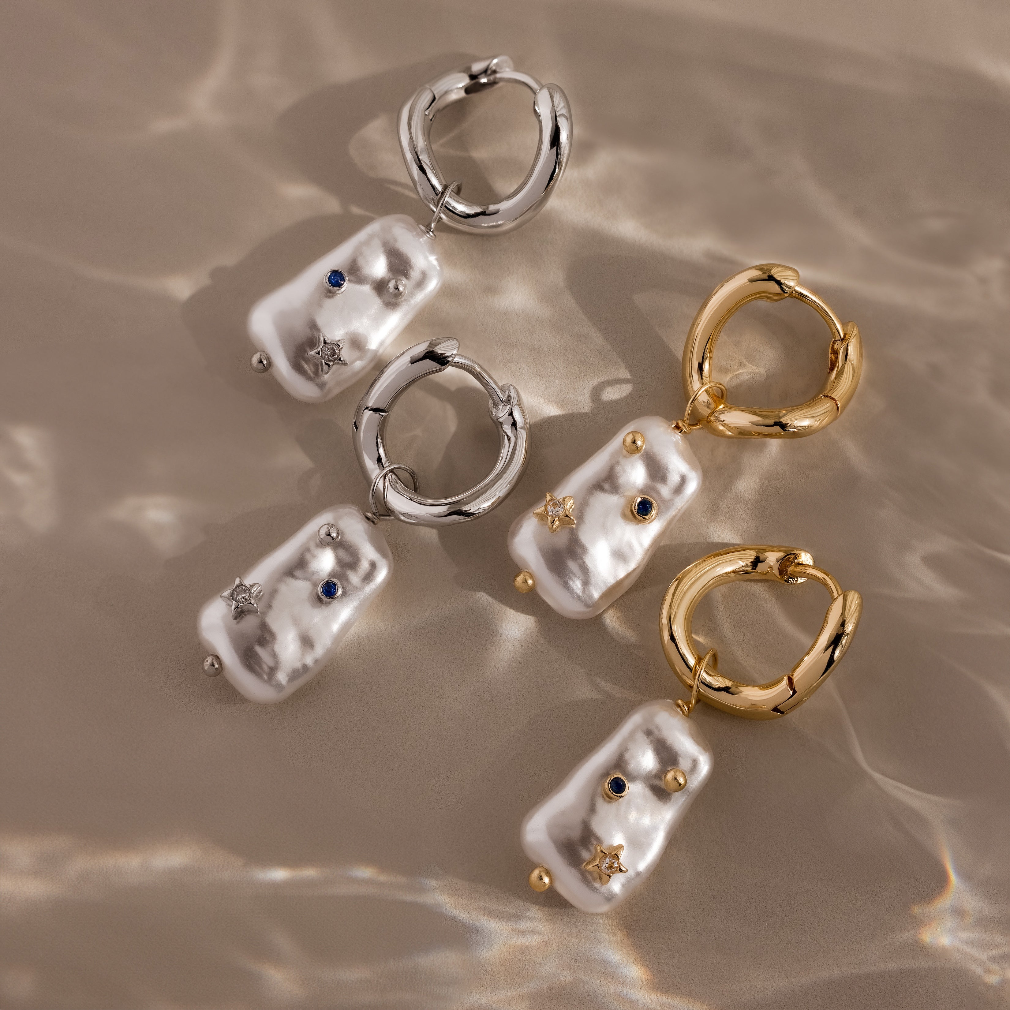 Starry Baroque Pearl Charm Hoops featuring pearl and gemstone accents are displayed on a beige, wavy surface.