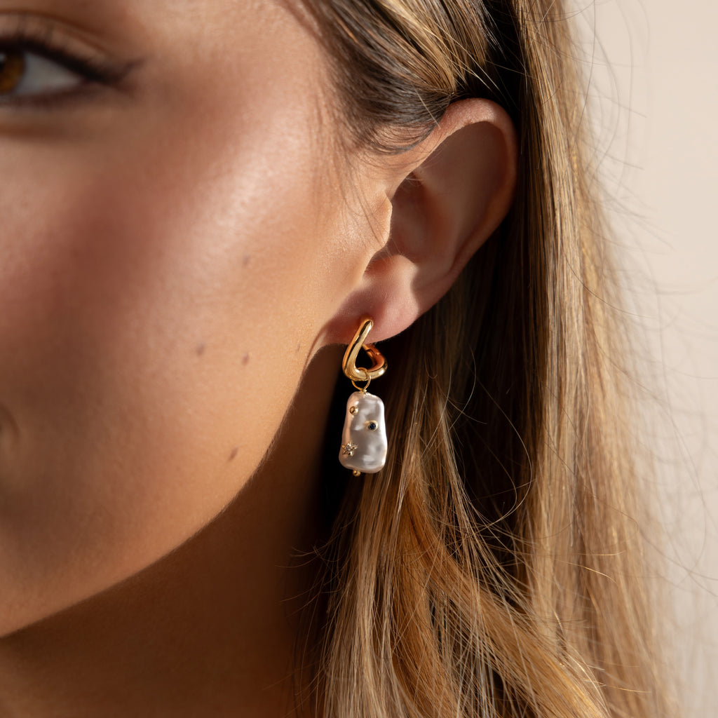 Close-up of a woman's ear wearing Starry Baroque Pearl Charm Hoops, featuring gold hoops with dangling Baroque pearl charms.