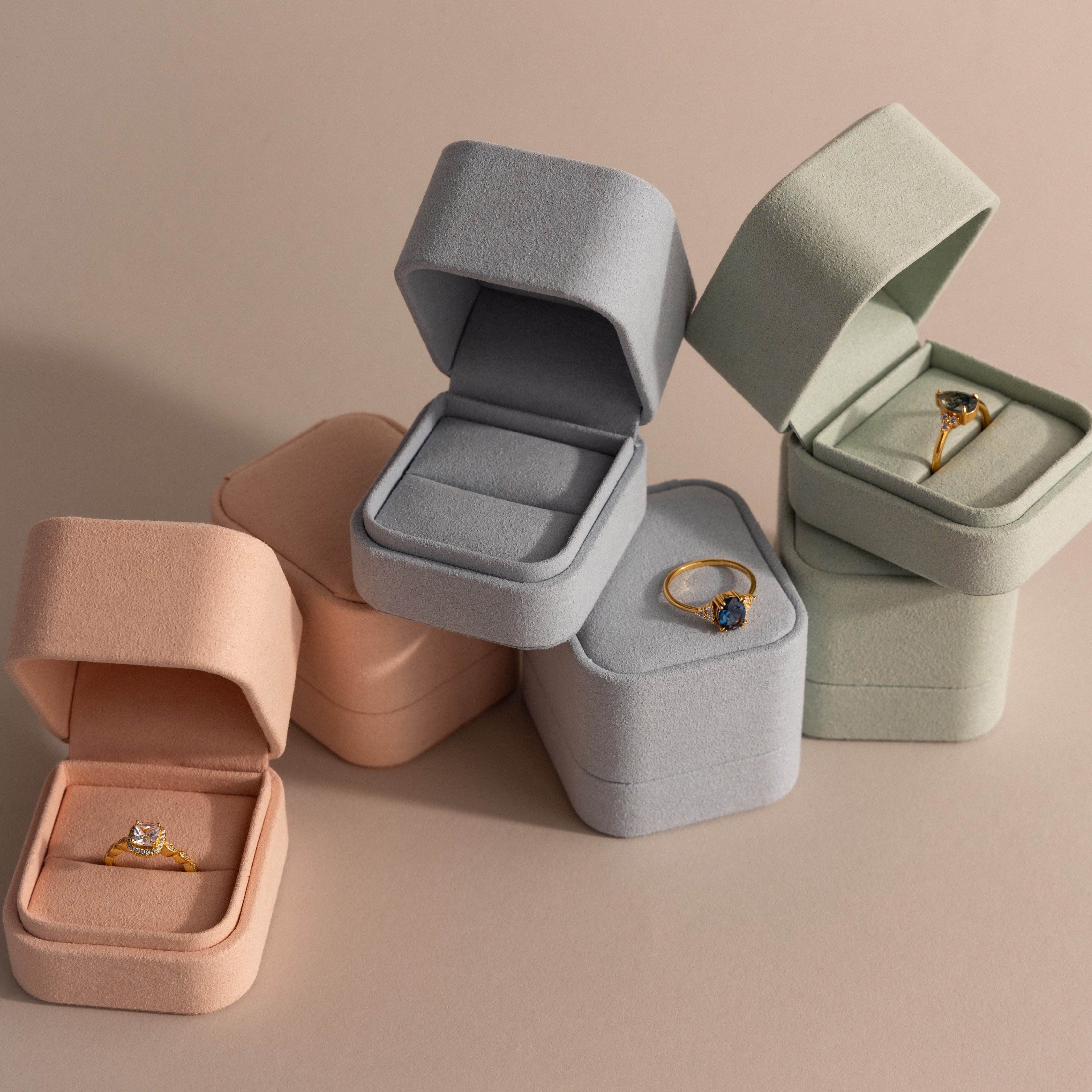 A Blue Suede Ring Box presents a gold gemstone ring on a neutral background, creating a minimalist and elegant display.