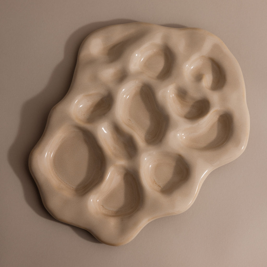 The Organic Treasure Trove Jewelry Dish is an irregular beige ceramic piece featuring multiple rounded indentations, ideal for displaying minimalist or organic jewelry against a neutral backdrop.