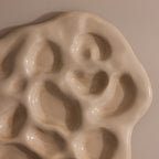 The Organic Treasure Trove Jewelry Dish features a cream-colored ceramic design with wavy edges and multiple oval indents, perfect for displaying your favorite pieces on any beige surface.