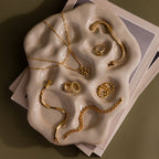 Gold jewelry pieces rest on the Organic Treasure Trove Jewelry Dish, which sits atop stacked papers against a muted backdrop.