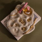 The Organic Treasure Trove Jewelry Dish displays gold jewelry, a pink perfume bottle, and lip gloss on stacked books for a chic minimalist look.