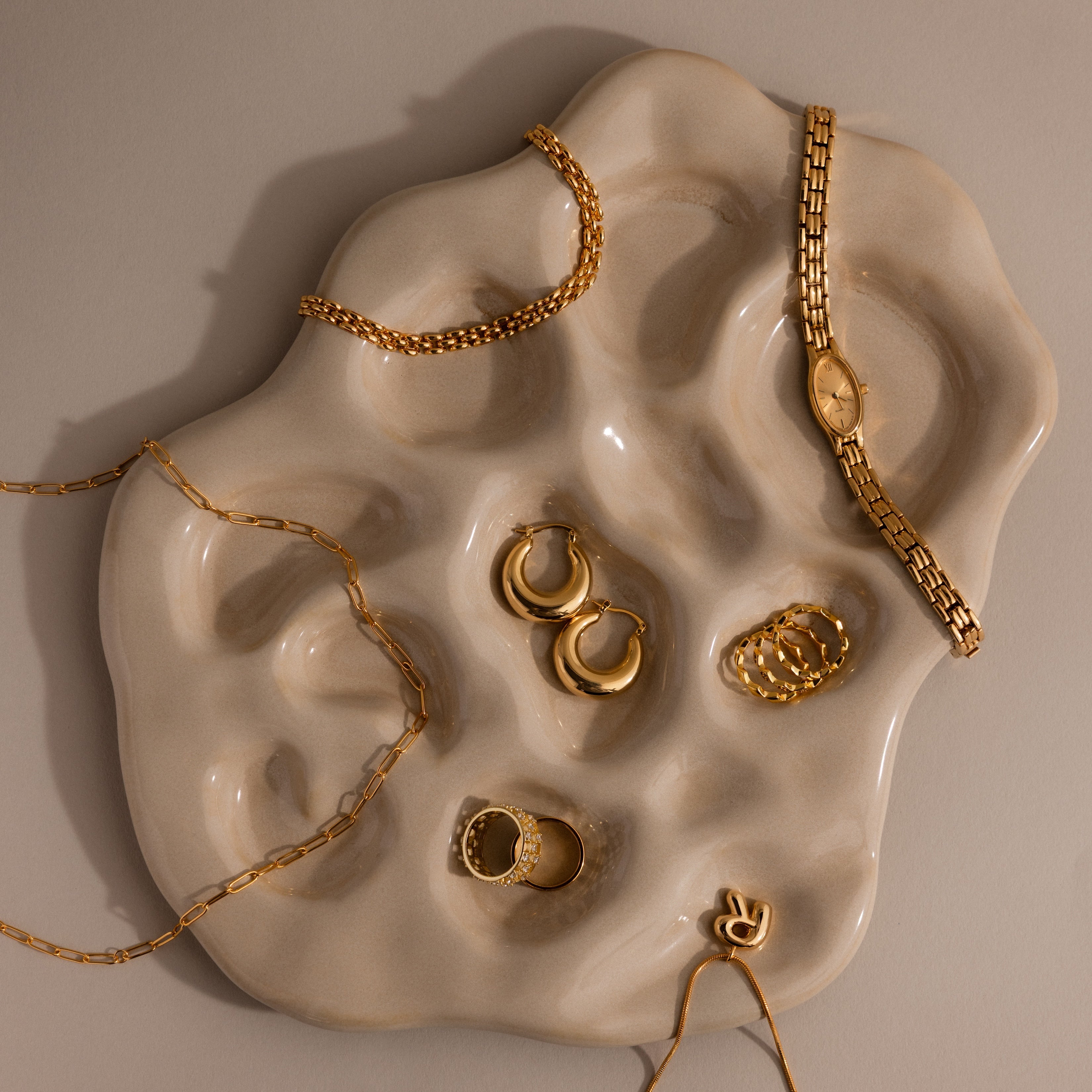 Gold jewelry and a gold watch elegantly displayed on the Organic Treasure Trove Jewelry Dish against a neutral background.