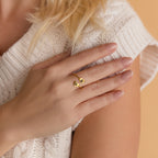 A hand with nude nails wearing a gold Paw Print Duo Heart Ring rests on a white knit sweater—the perfect gift for pet lovers.