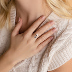 Close-up of a woman's hand wearing the Paw Print Duo Heart Ring, resting on her chest over a cream cable knit sweater.