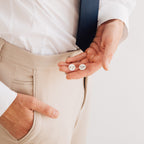 A man in beige pants and a tie holds two Engraved Cufflinks, one personalized with "SUPER DAD.