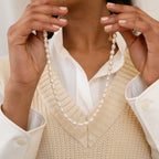 A person wearing a cream knitted vest over a white button-up shirt showcases the Bold Pearl Necklace.