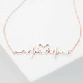 The Heartbeat Necklace in rose gold features a heartbeat line with a central heart, shown on a white background—a unique, personalized gift for someone special.