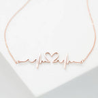 The Heartbeat Necklace in rose gold features a heartbeat line with a central heart, shown on a white background—a unique, personalized gift for someone special.