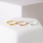 The Stacking Name Band features three custom engraved rings in gold, rose gold, and silver—shown with Jasmine, Jasper, and Finn—on a white surface. Ideal personalized jewelry for any meaningful occasion.