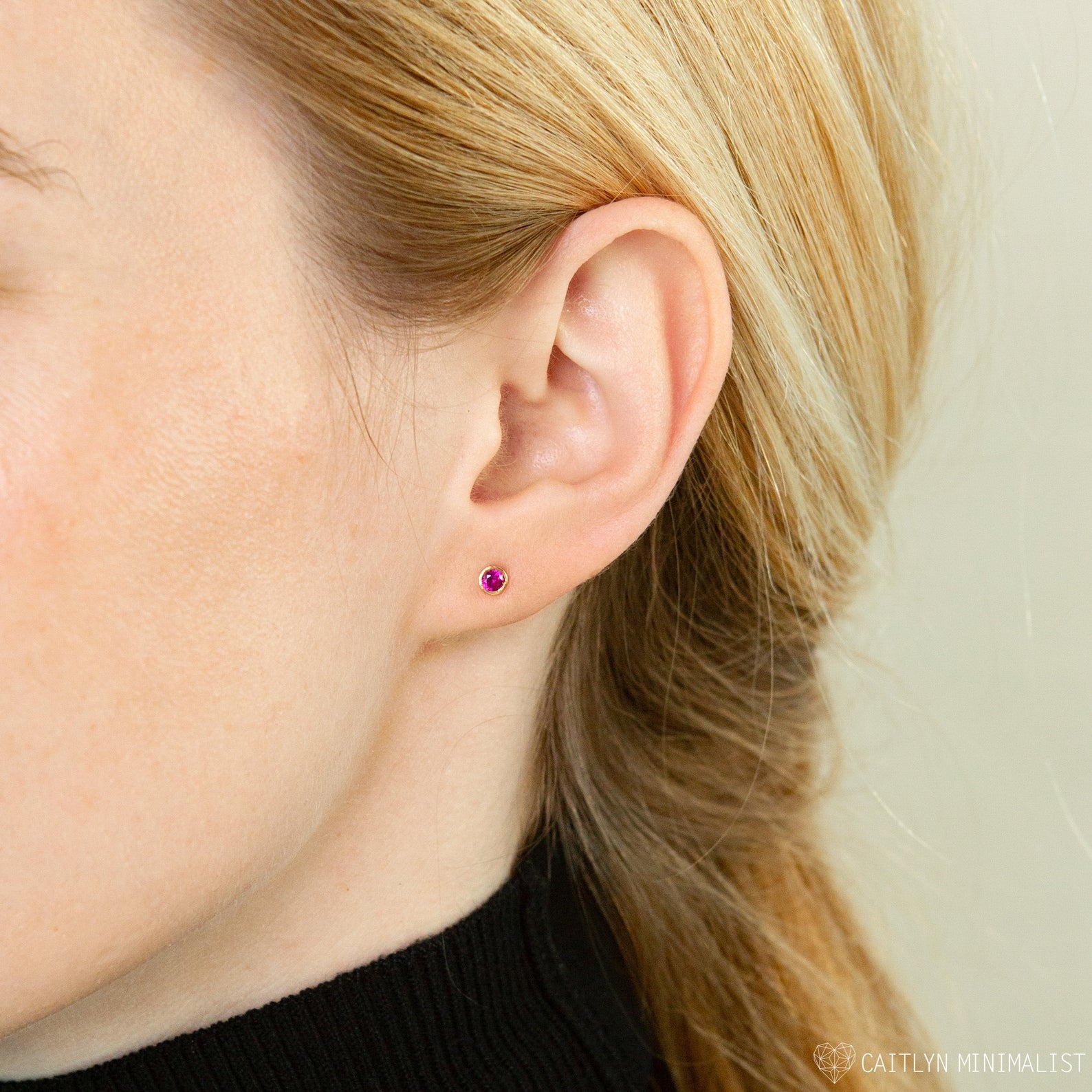 Close-up of a woman with blonde hair pulled back, wearing Birthstone Studs—a small pink earring perfect for everyday wear.