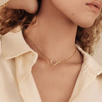 Minimalist gold chain necklace featuring a circle shaped toggle clasp, worn close to the neck for a modern, elegant look. Styled with an ivory button down shirt.
