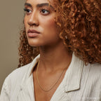 A portrait of a woman wearing a gold curb chain necklace with a cream textured blouse, highlighting the necklace’s delicate shine.