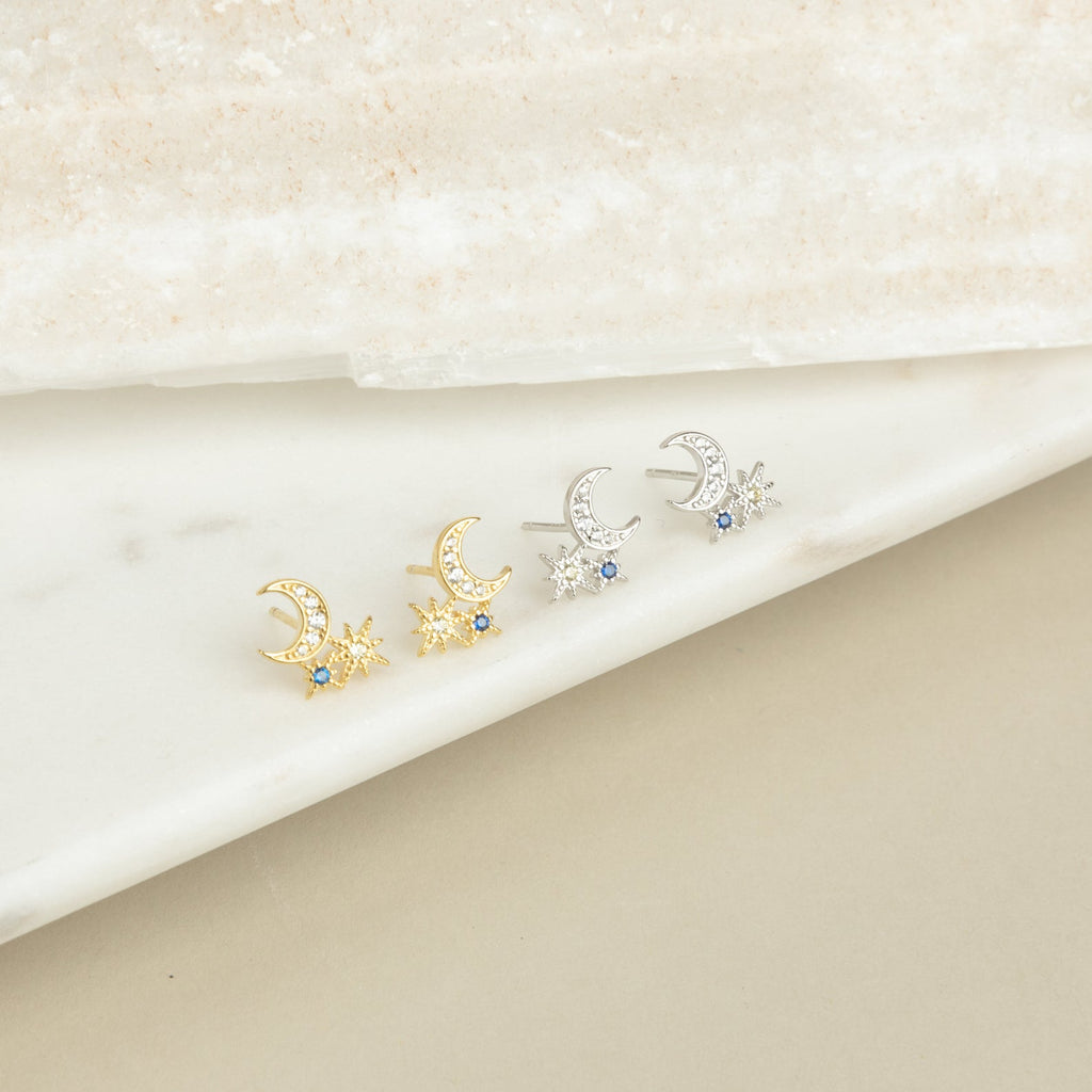 Two pairs of Aeon Studs—crescent moon and star earrings in gold and silver—displayed on marble, perfect for constellation earring lovers.