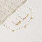 Three gold necklaces with letter charms are shown on a light textured surface; one is a stylish Mama Necklace—perfect for gifting—while the others spell MAVERICK and feature individual letters M, A, R, and I.
