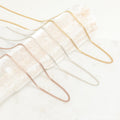 A variety of curb chain necklaces in gold, silver, and rose gold finishes displayed draped across a textured cream prop.