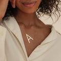 Woman wearing a Large Sideways Initial Necklace featuring a bold gold letter pendant, styled with a cream blouse for a standout look.