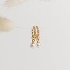 Mae Huggies: Elegant gold pearl earrings with sparkling crystals, delicately hanging on a string against a light background.