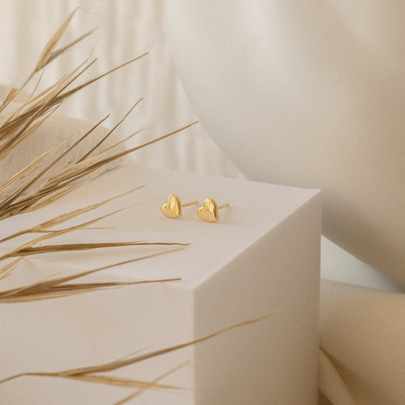 Classic Heart Studs are displayed on a white geometric surface, with dried grass in the foreground, highlighting their delicate and cute design.