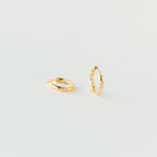 The Kaia Diamond Huggies are small gold hoop earrings with clear stones, adding subtle sparkle. Their dainty diamond design is beautifully showcased against a plain white background.