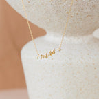 The Mrs. Necklace features a gold pendant spelling mrs in cursive, displayed on a textured white surface—an elegant wedding gift idea for the newlywed bride.