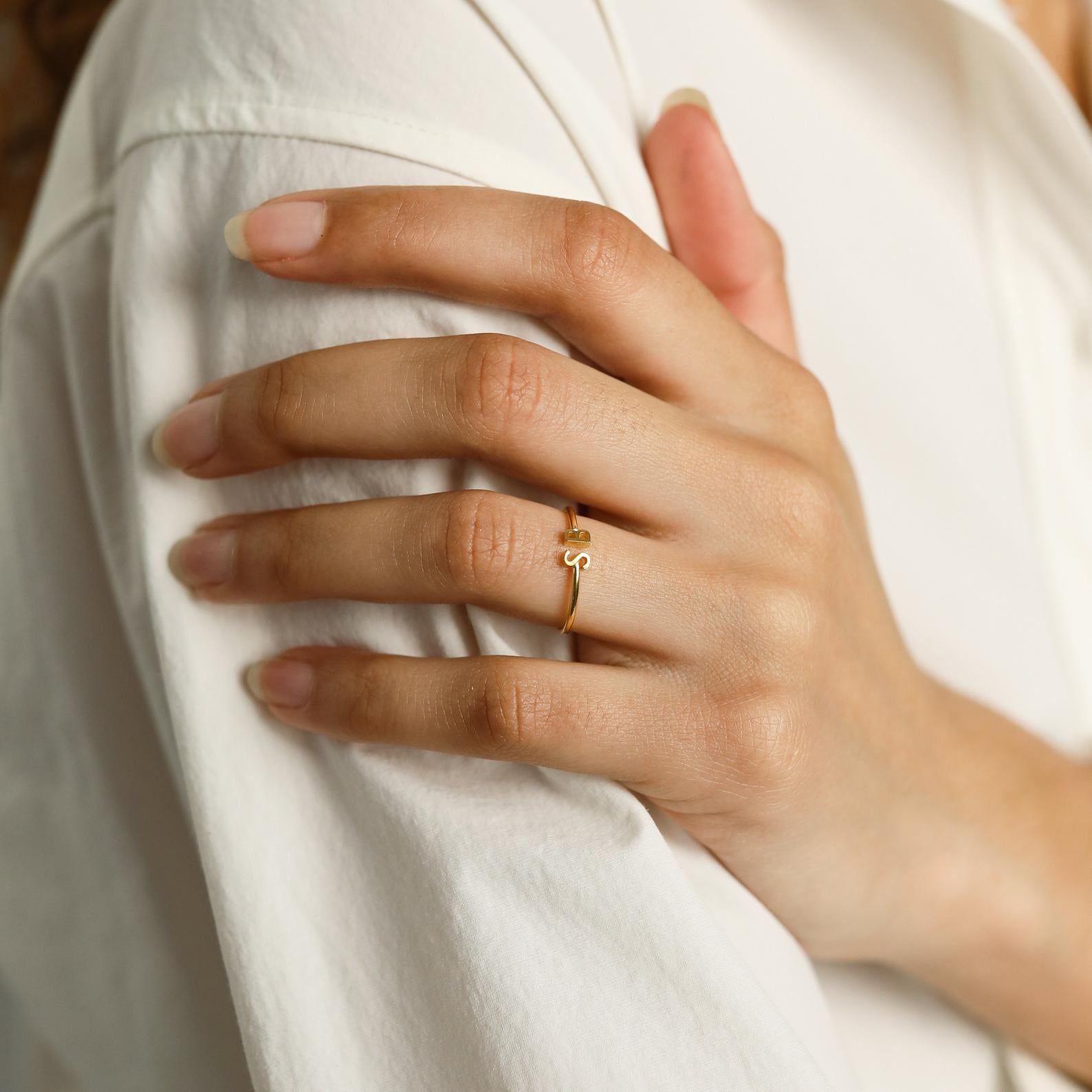 A hand with natural nails wears the Modern Duo Initial Ring, a delicate personalized piece, resting on a white shirt sleeve.