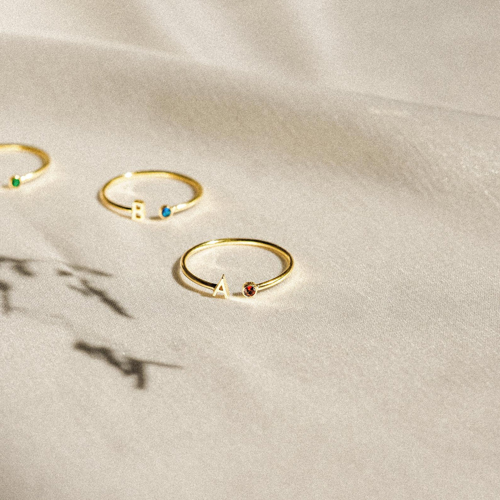 Modern Initial Birthstone Rings with colored stones and letter charms A and B displayed on a light textured fabric—these customizable rings make a thoughtful Christmas gift.
