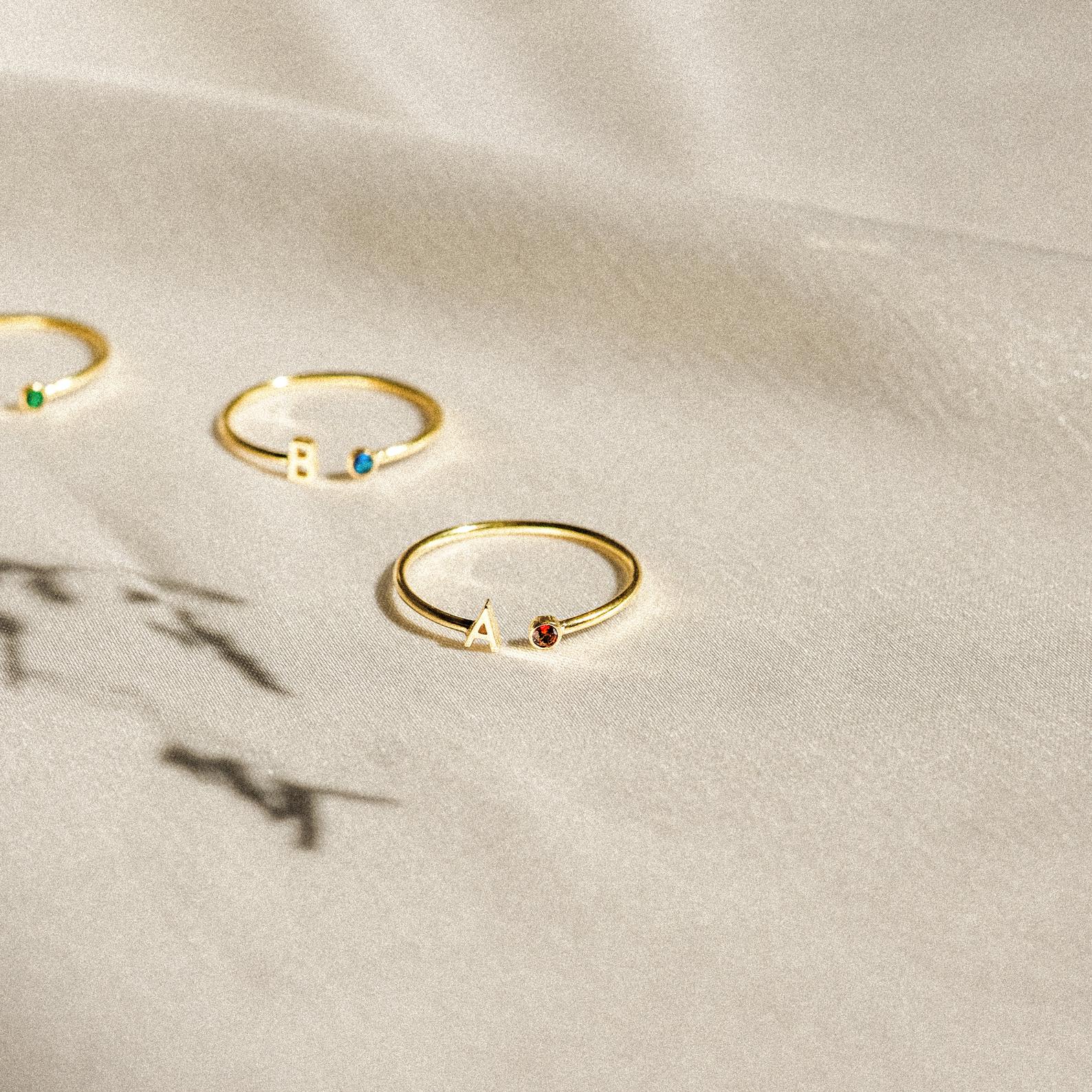 Modern Initial Birthstone Rings with colored stones and letter charms A and B displayed on a light textured fabric—these customizable rings make a thoughtful Christmas gift.