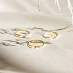 Three gold Venice Initial Birthstone Rings rest on light fabric, each with a delicate gemstone and cursive lowercase letter charm—a personalized ring, perfect as an initial birthstone accessory for everyday elegance.