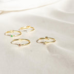 Four delicate Zodiac Birthstone Rings with colorful gemstones are displayed on soft ivory fabric, creating an elegant jewelry statement.