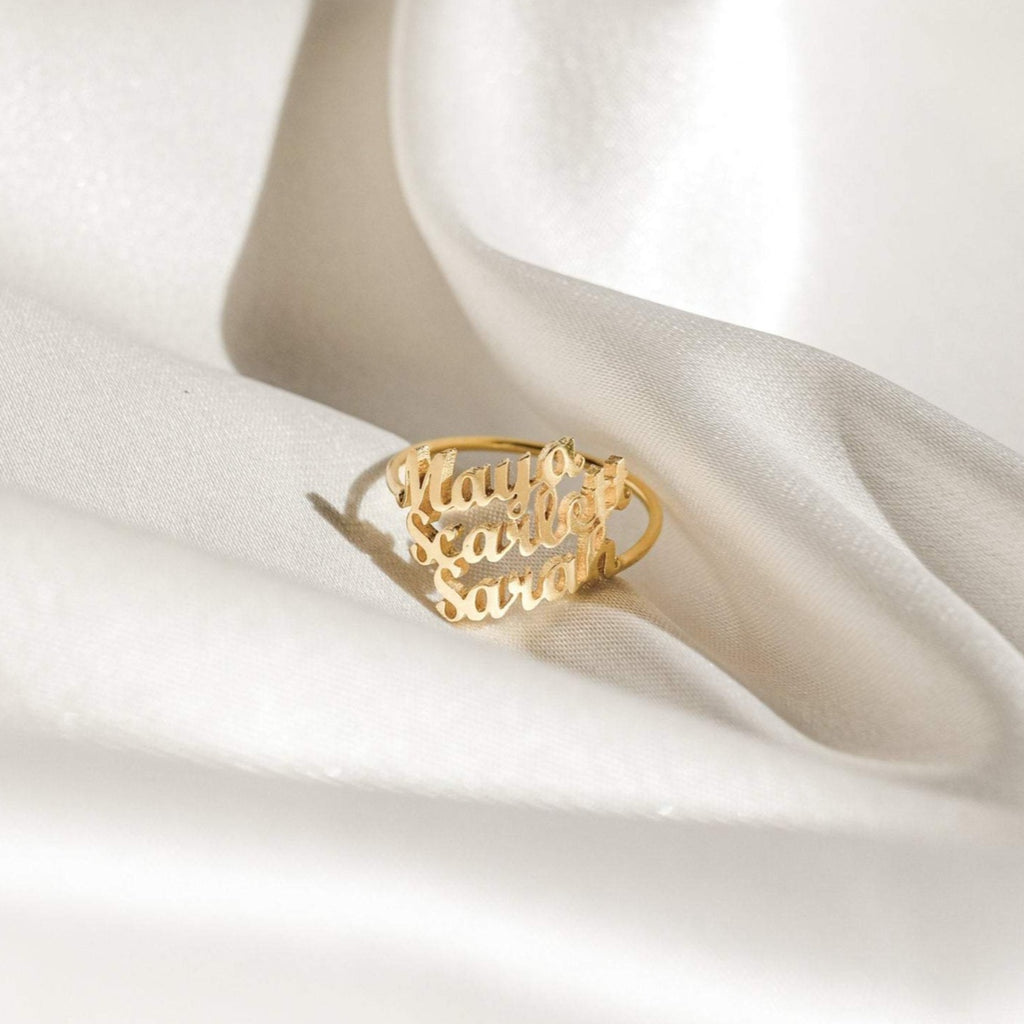 London Triple Name Ring with Mauro, Scarlet, and Sarah engraved, displayed on white satin fabric—a stunning piece of personalized jewelry.