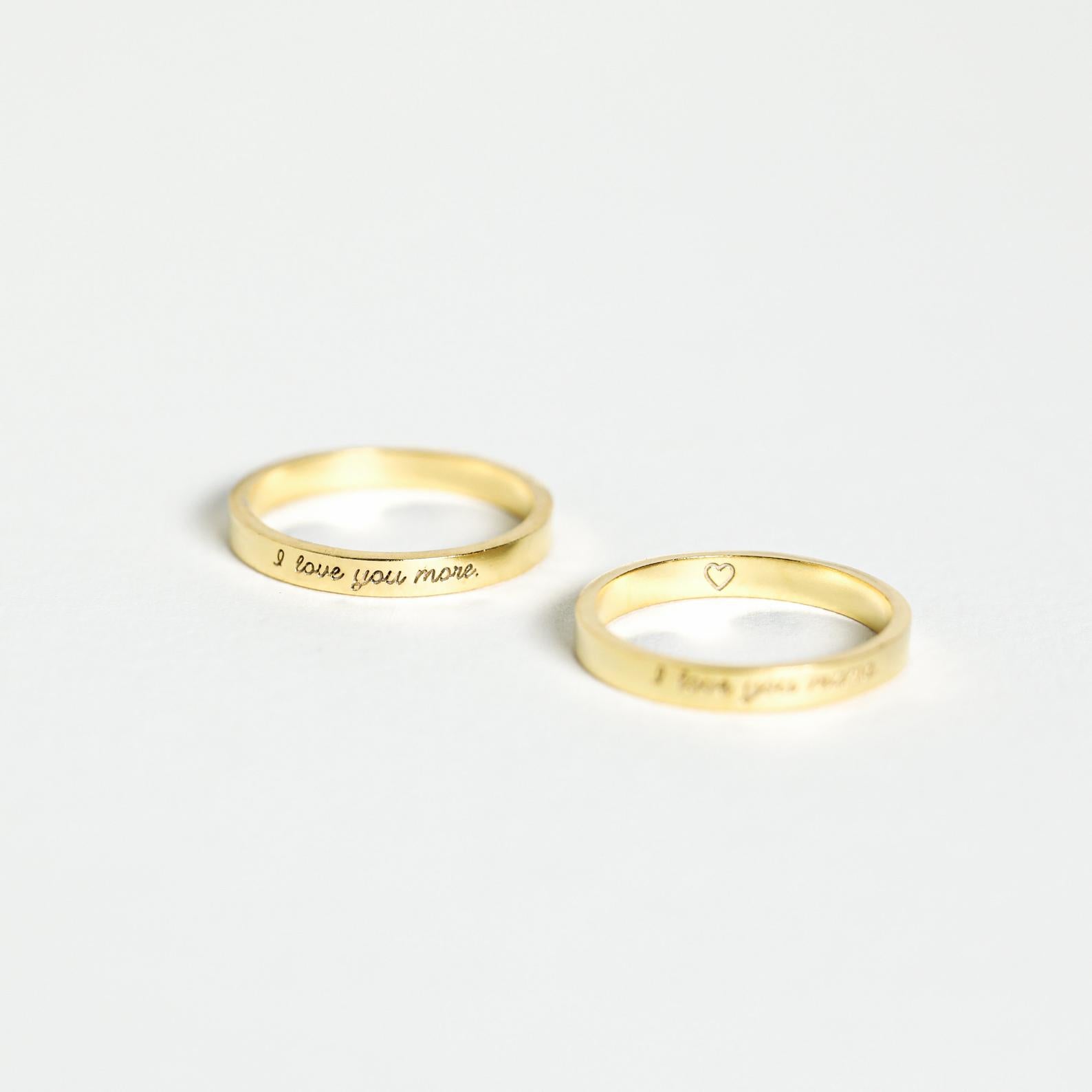 The Ann Thin Message Ring set includes two simple gold engraved rings—one reads "I love you more," and the other features a small heart. A personalized, thoughtful holiday gift perfect for couples.