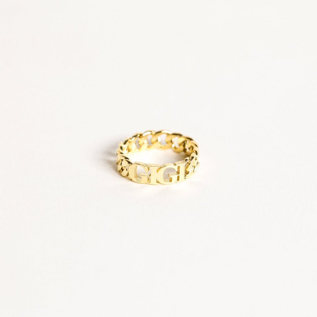 The Newsletter Curb Name Ring in Rose Gold features a gold chain design with personalized letters at the center, showcasing the classic curb name ring style against a plain white background.