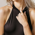 Woman in a sleeveless black top holds her collar, wearing the contemporary Tia Twisted Ring and showcasing a subtle finger stack, with a small finger tattoo adding to her chic look.